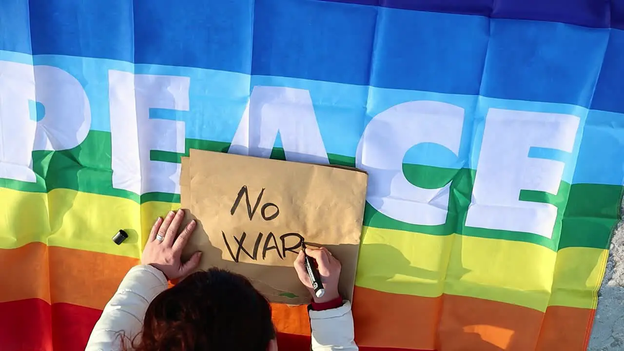 Female caucasian hand writes anti-war protest placard zoom out close up shot