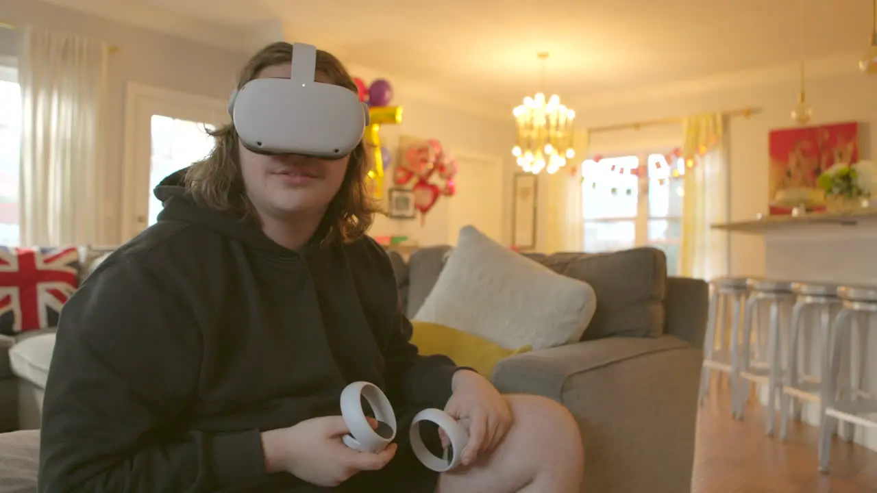 Teenage boy at home wearing a virtual reality headset and holding controllers gazes into a simulated world