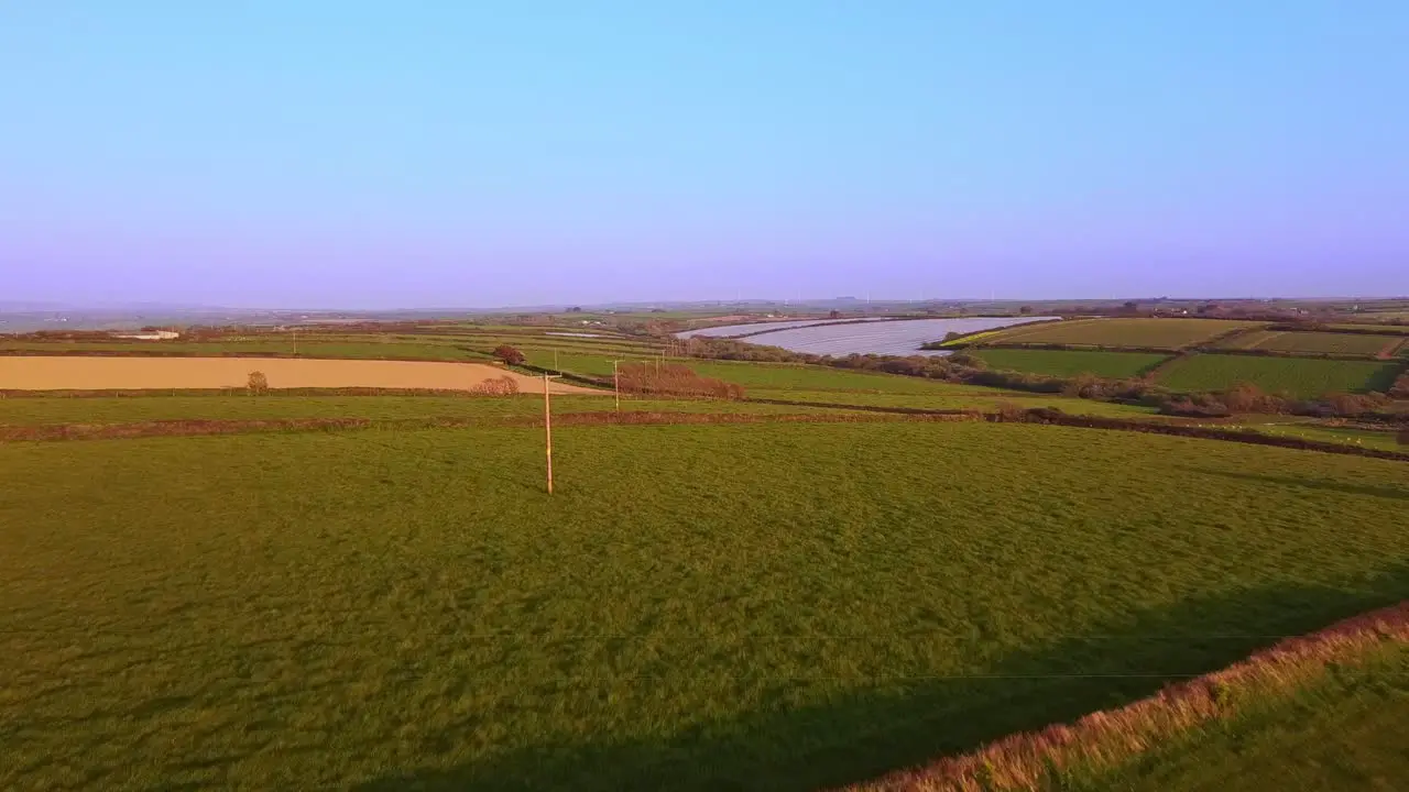 Aerial drone tracking phoneline mast through a field during sunset