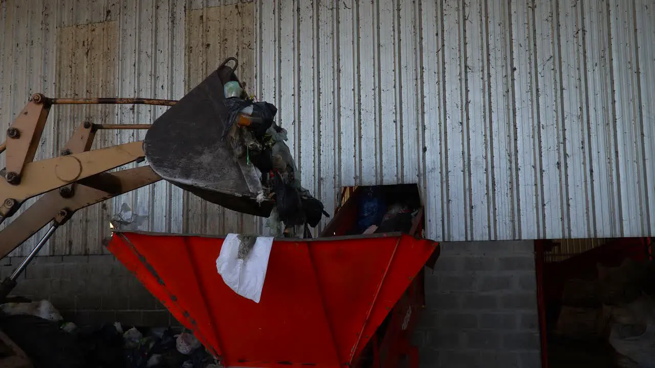 A bulldozer's bucket throws the waste into a conveyor belt's hopper inside a waste processing plant