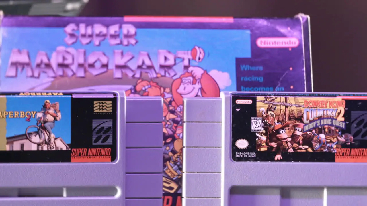 Vintage Super Nintendo Cartridges with Box in Background in Purple Light SLIDE RIGHT