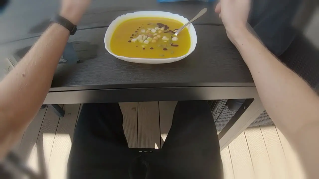 POV first person eating orange pumpkin soup outside