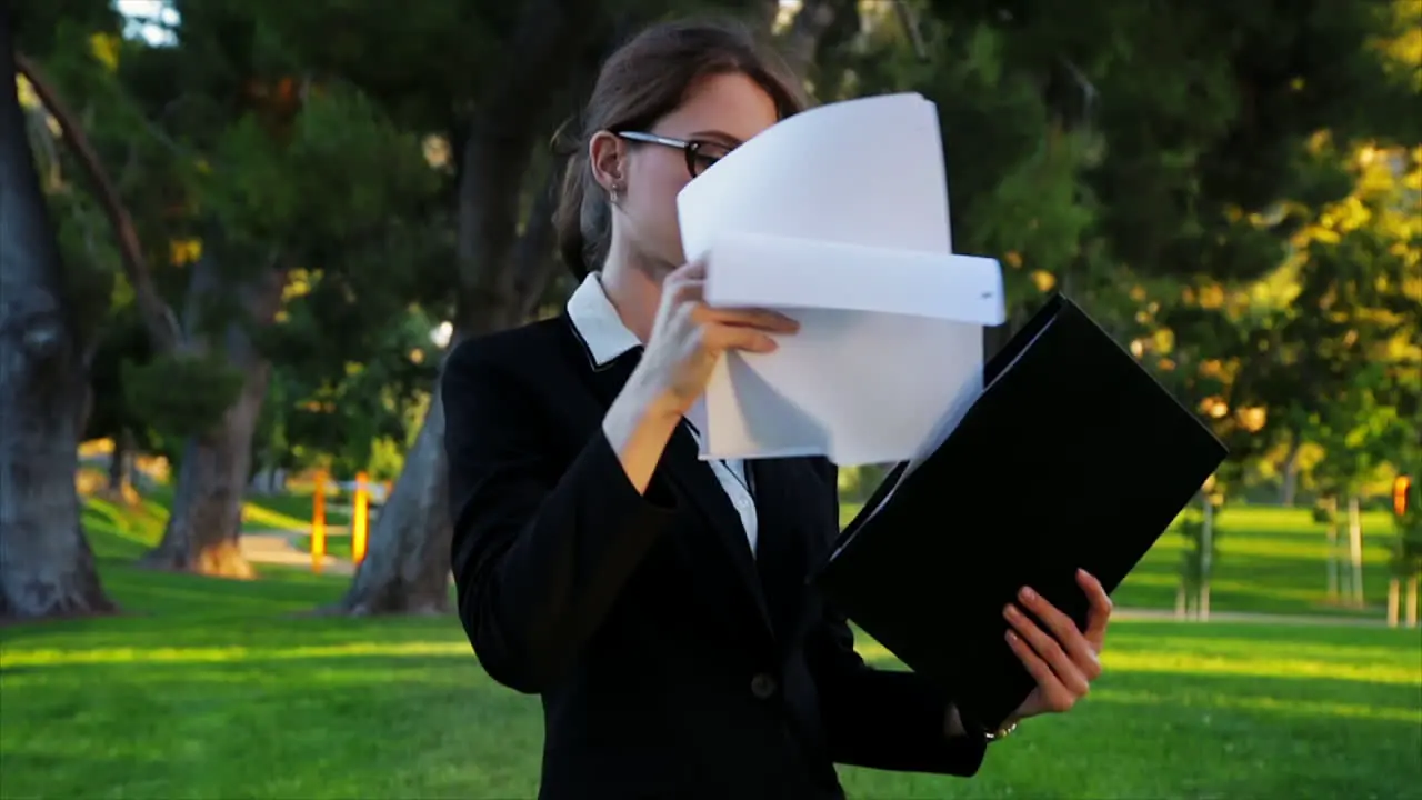 Attractive caucasian business woman flips through paperwork in her folder takes a look at a document checks her watch and then exits