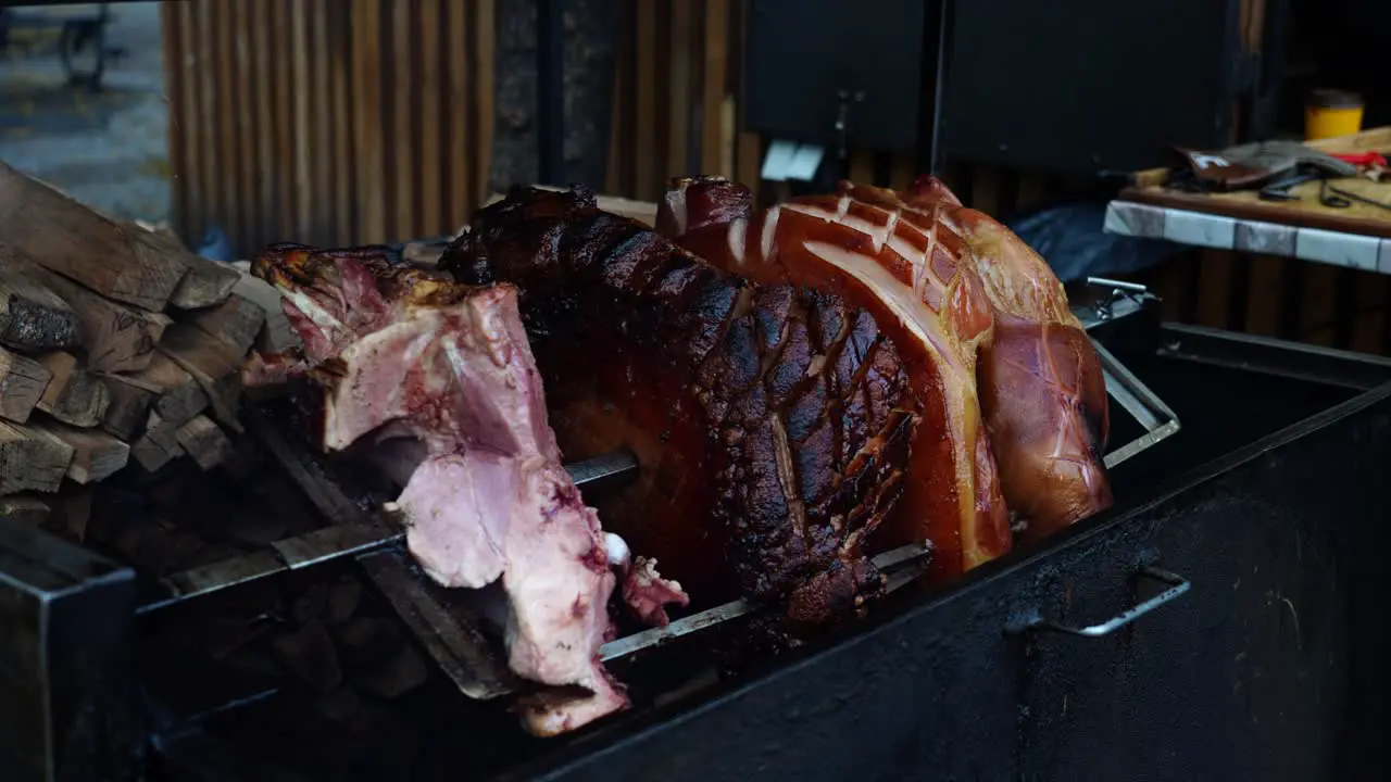 Juicy beechwood smoked ham rotate above grill on skewer near firewood