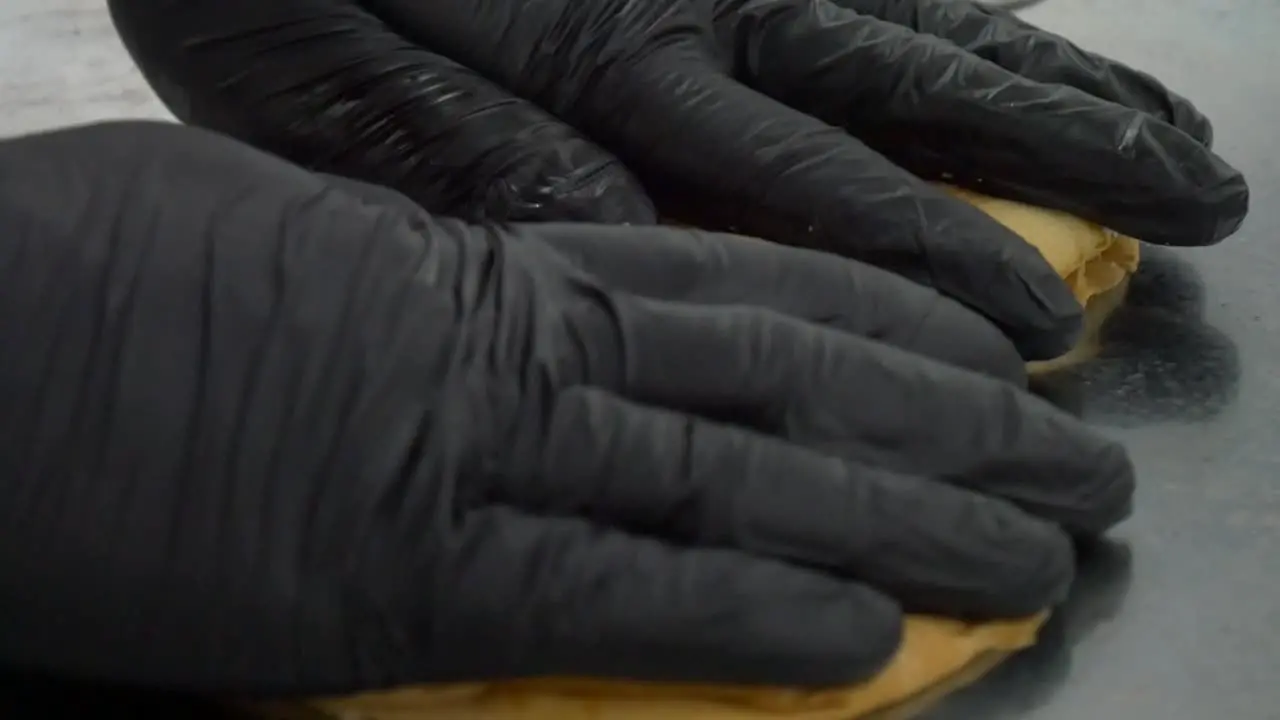 Hamburger bun is placed on a restaurant grill by the gloved hands of a chef