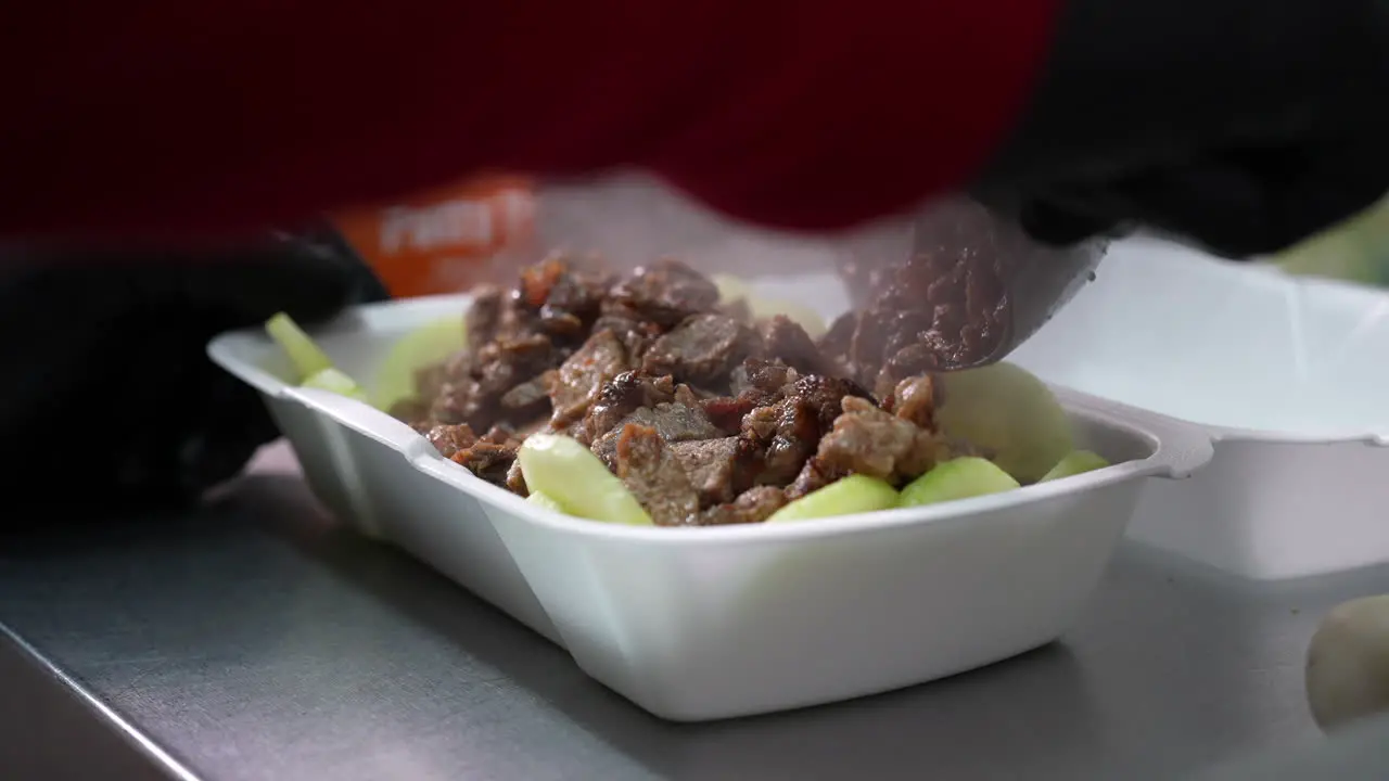 Adding the chopped grilled steak to the cucumbers in a keto bowl food truck series