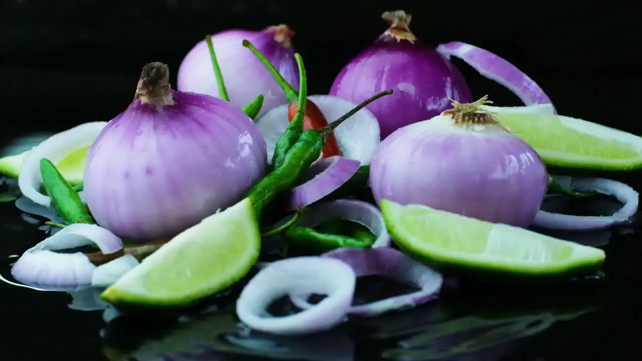 Onion Rings Falling onto other Onions Lime Quarters and Chili Peppers on a Wet Black Surface