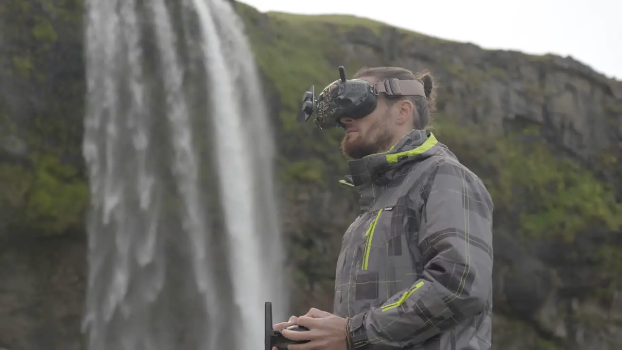 Man controls an FPV drone for aerial photography and video with a remote control and goggles behind a waterfall in Iceland