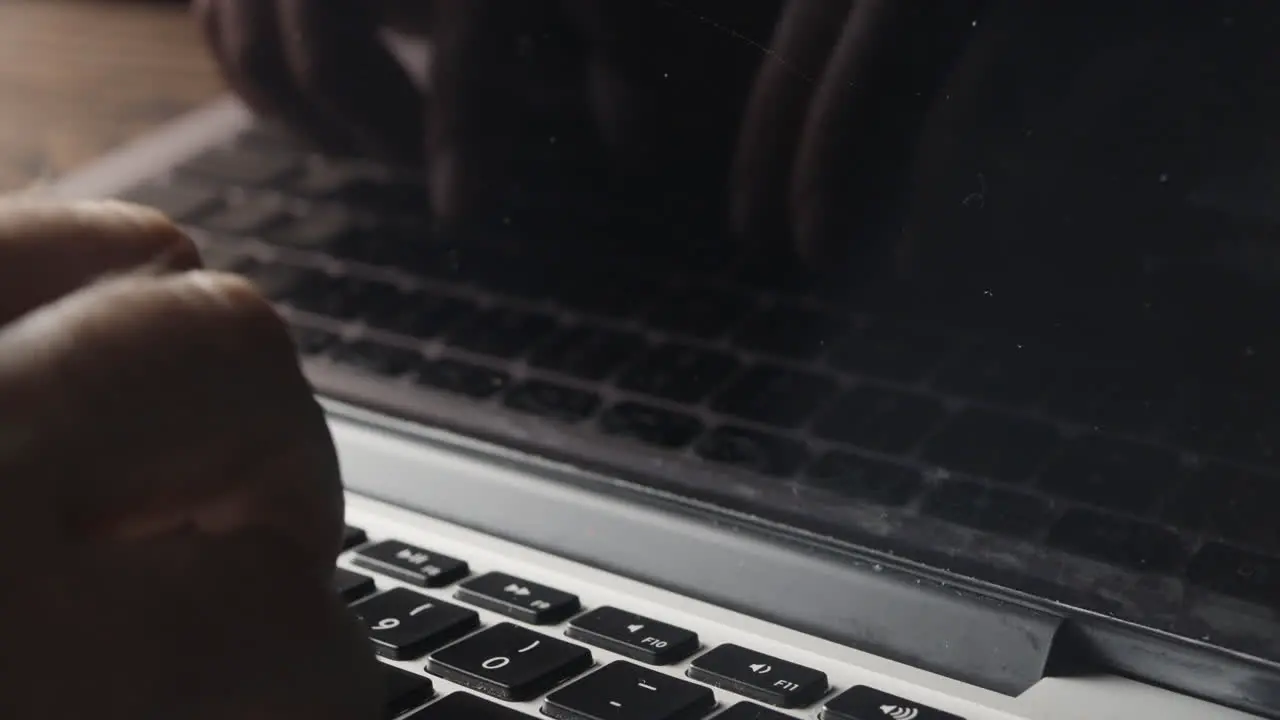 Hand Typing on Laptop Keyboard with Reflection Mirrored in Screen