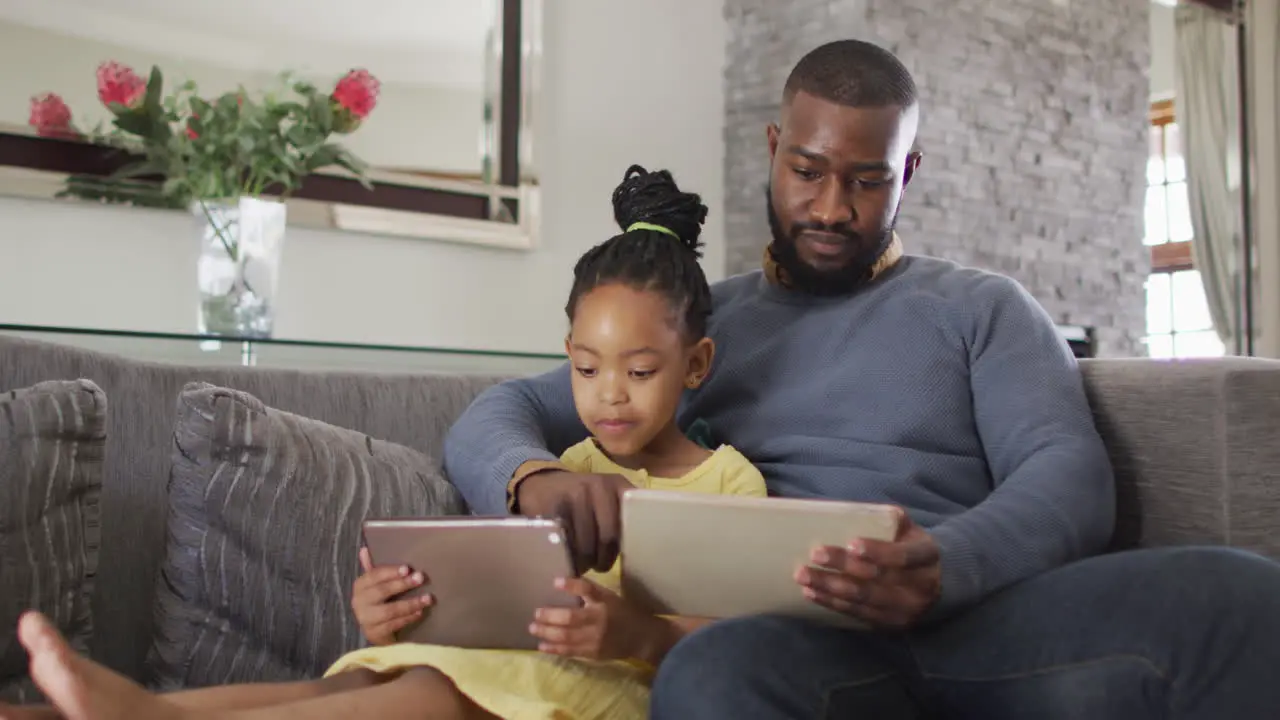 Happy african american daughter and father using tablets on sofa