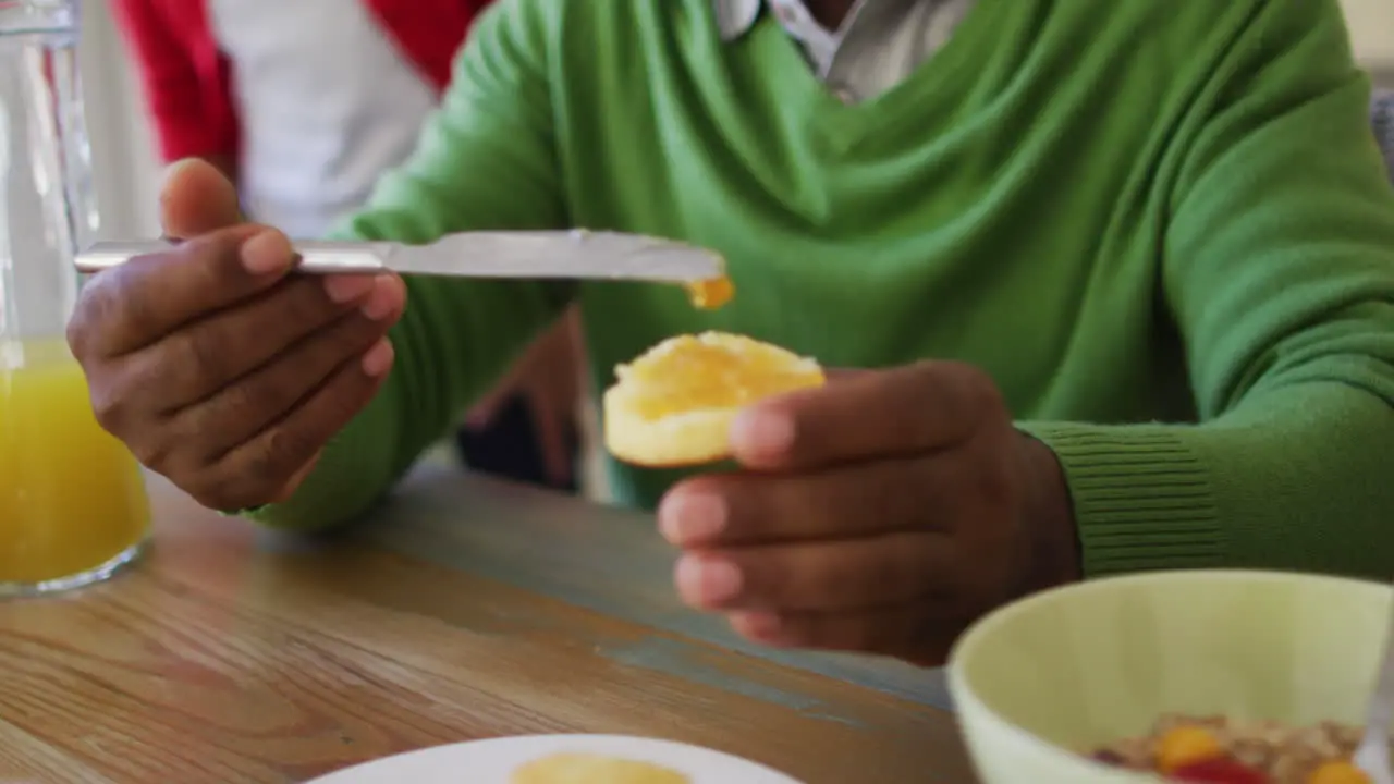 African american senior man applying jam oh his bread while having breakfast with family at home