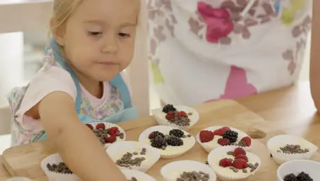 Cute little girl putting berries on muffins