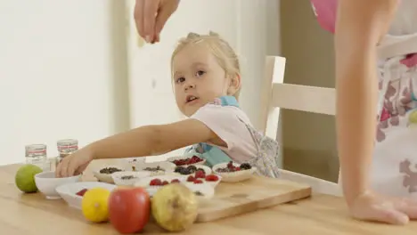 Child watching woman sprinkle candy on muffins