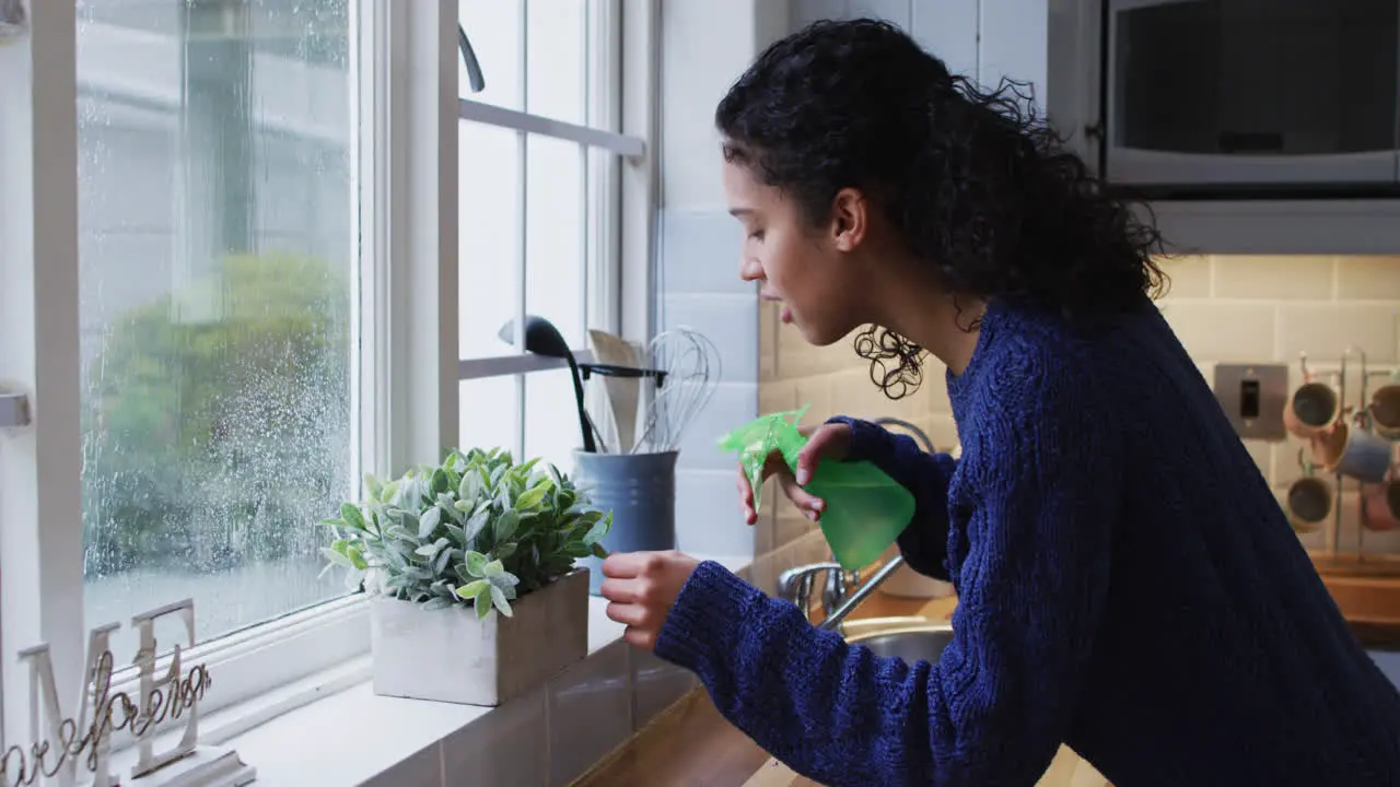 Mixed race woman watering plants in kitchen