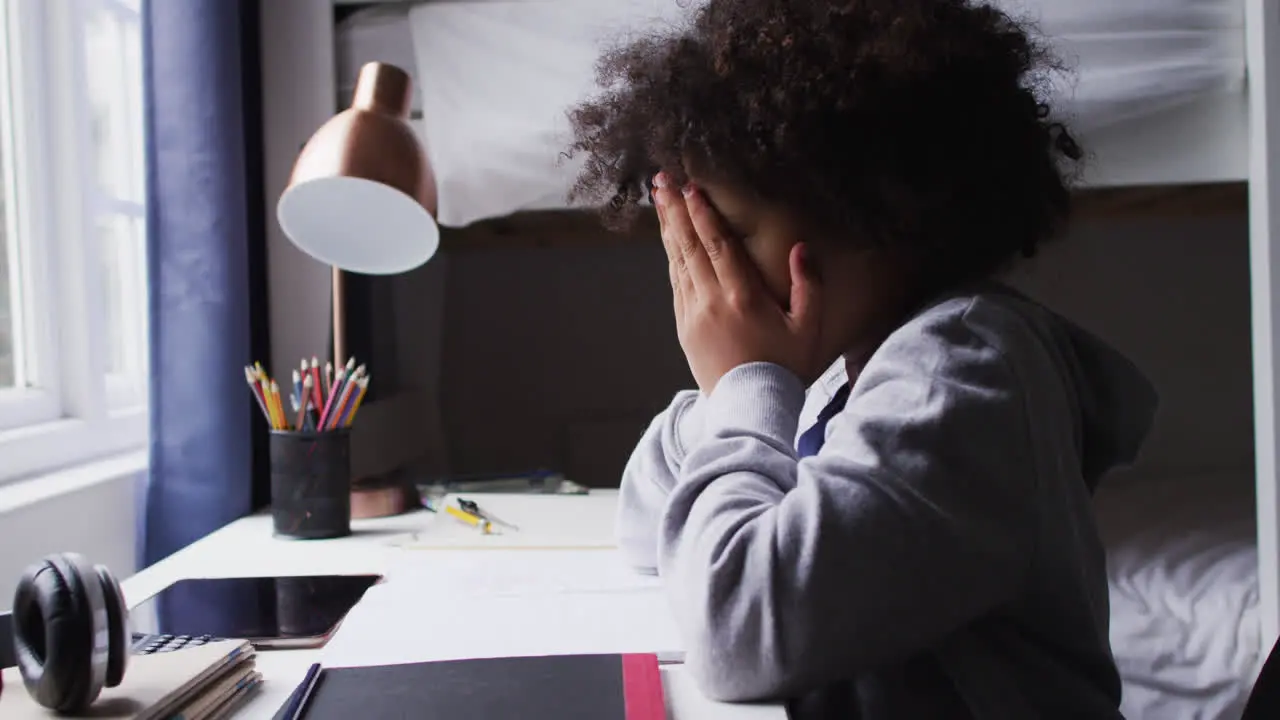 Mixed race girl sitting by desk covering her eyes