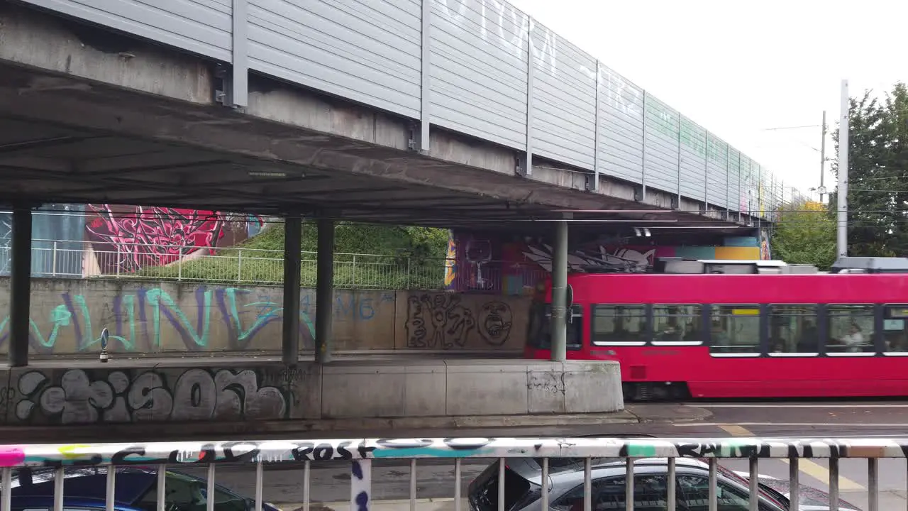 A Red Tram Car Drives under a bridge Street with gratifies in Bern Switzerland