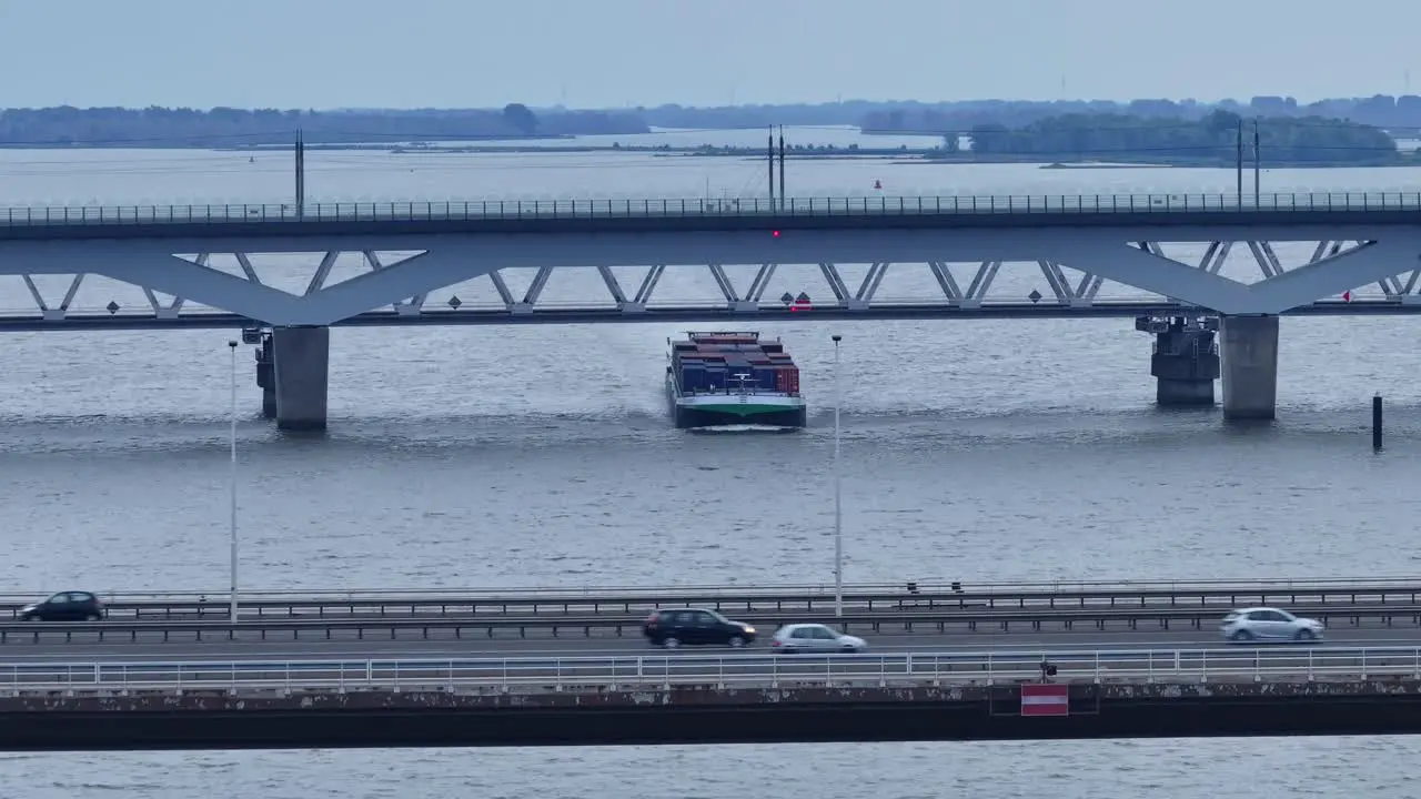 Drone view of a container ship sailing under the Alfa Menta Moerdijk bridge with passing cars in the Netherlands