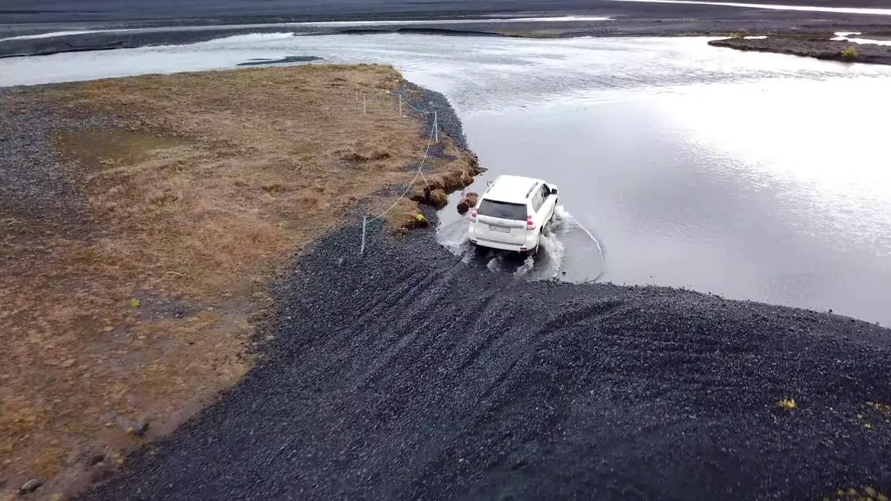 4WD white rental SUV crossing a glacial river in deep water on volcanic sand and rock aerial trucking shot