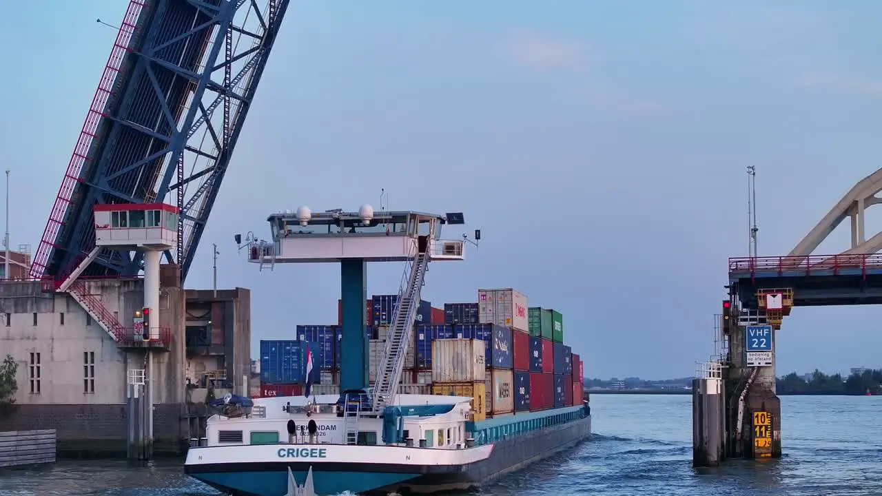 Cargo ship with containers sails over a raised bridge on a river