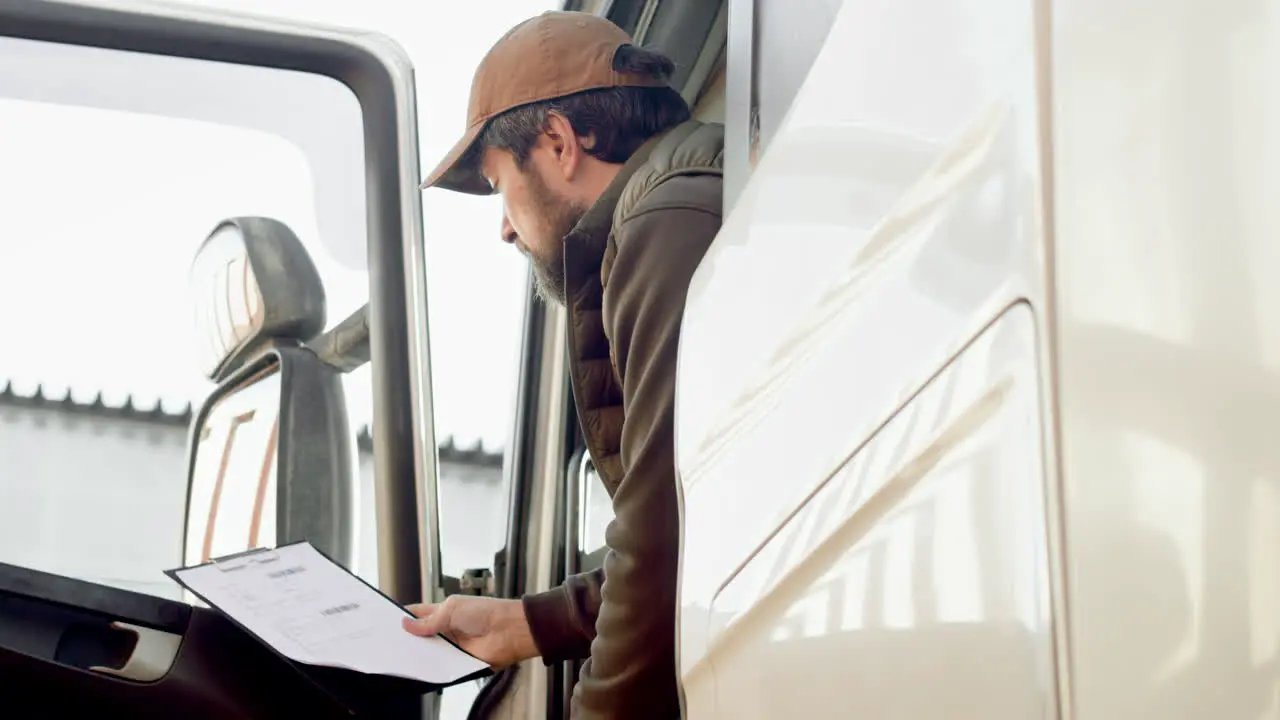 Worker Wearing Vest And Cap Organizing A Truck Fleet In A Logistics Park While Reading Documents In A Truck 2