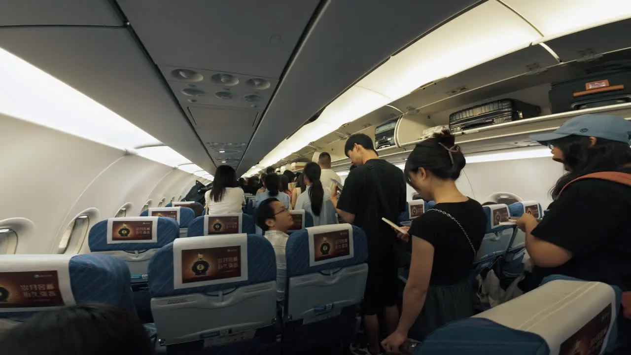 Asian passengers standing in airplane walk way aisle waiting for disembarkation