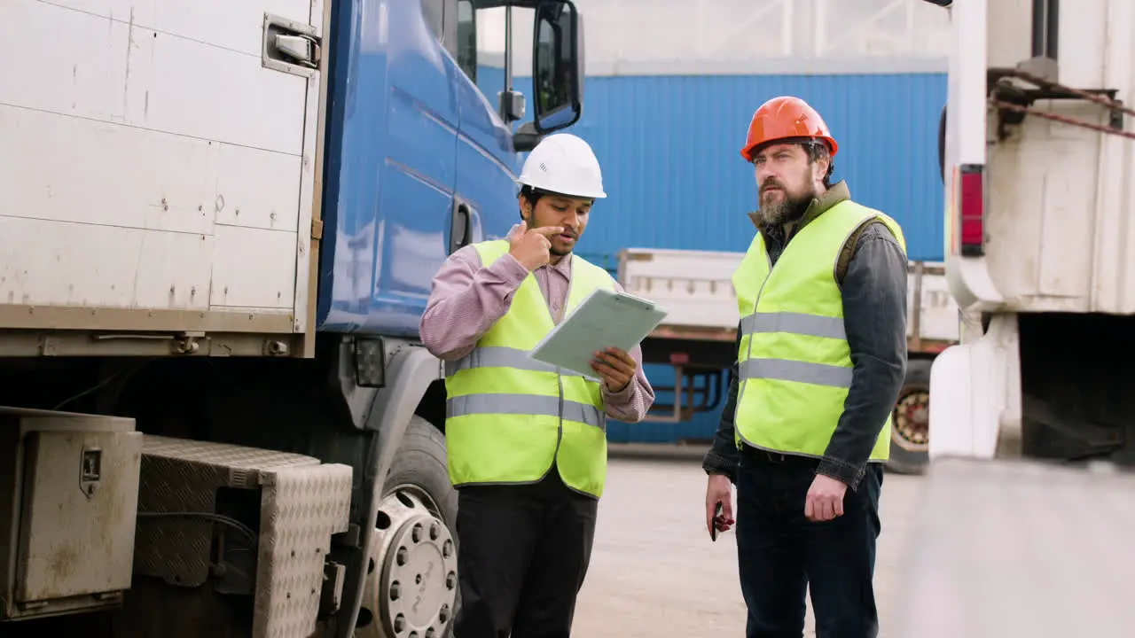 Boss And Worker Wearing Vests And Safety Helmets Organizing A Truck Fleet In A Logistics Park While They Consulting A Document 4