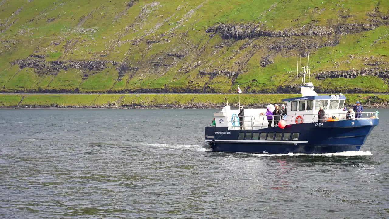 Blue and white boat with a Faroese flag drives in waters of Mykines to Sorvagur in Vagar Island