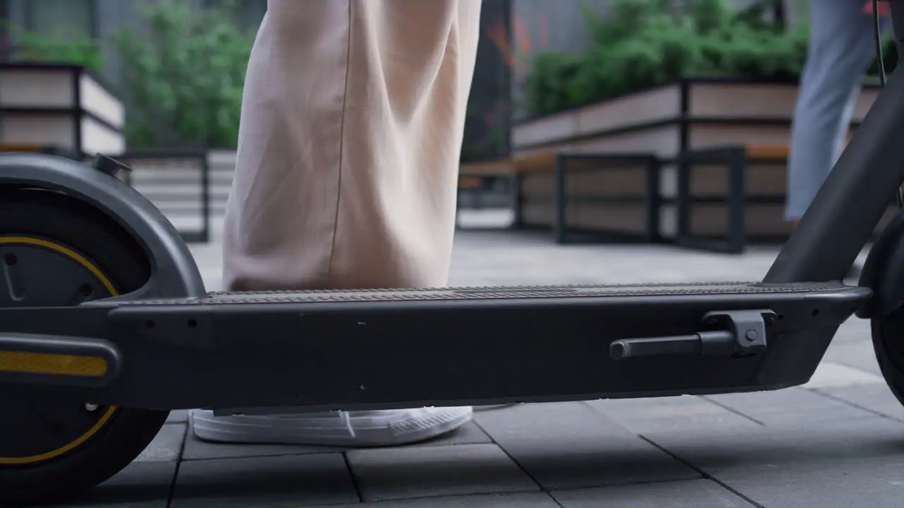 Woman legs riding kickscooter in white sneakers going away at downtown closeup