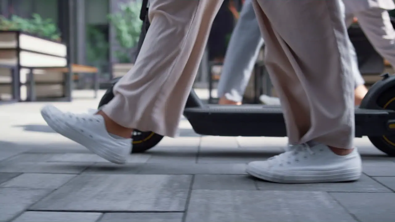 Closeup female legs walking with electric scooter at downtown street in morning