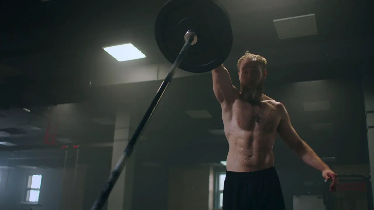 A male athlete lifts a weight bar with one hand in slow motion Strength training for a boxer The man is sweating working out in the gym practicing the force of the blow with his hand