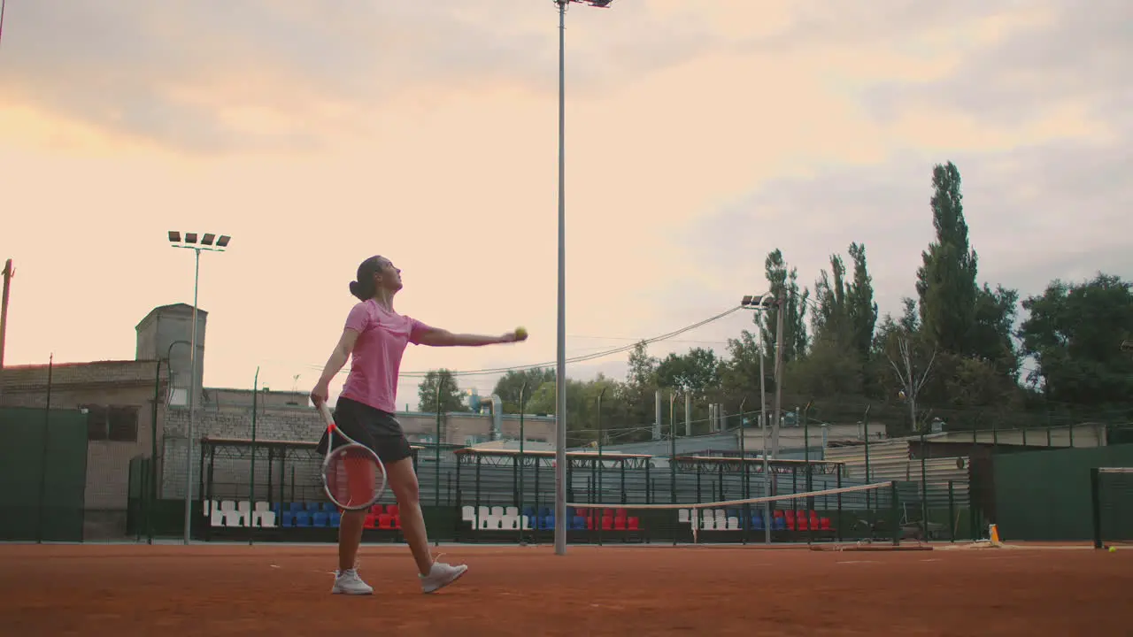 slow-motion side view of a young athlete trains the serve of the tennis ball A teenage athlete is playing tennis on a court An active girl is powerfully hitting a ball during sport practicing