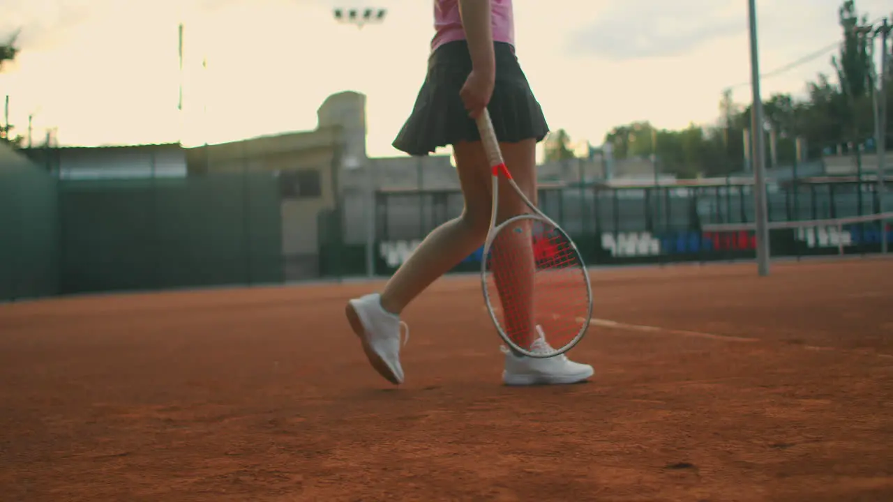 At tennis practice the girl approaches the central service line and prepares to serve knocks the ball several times on the ground and catches the ball with her hand long shot at ground level