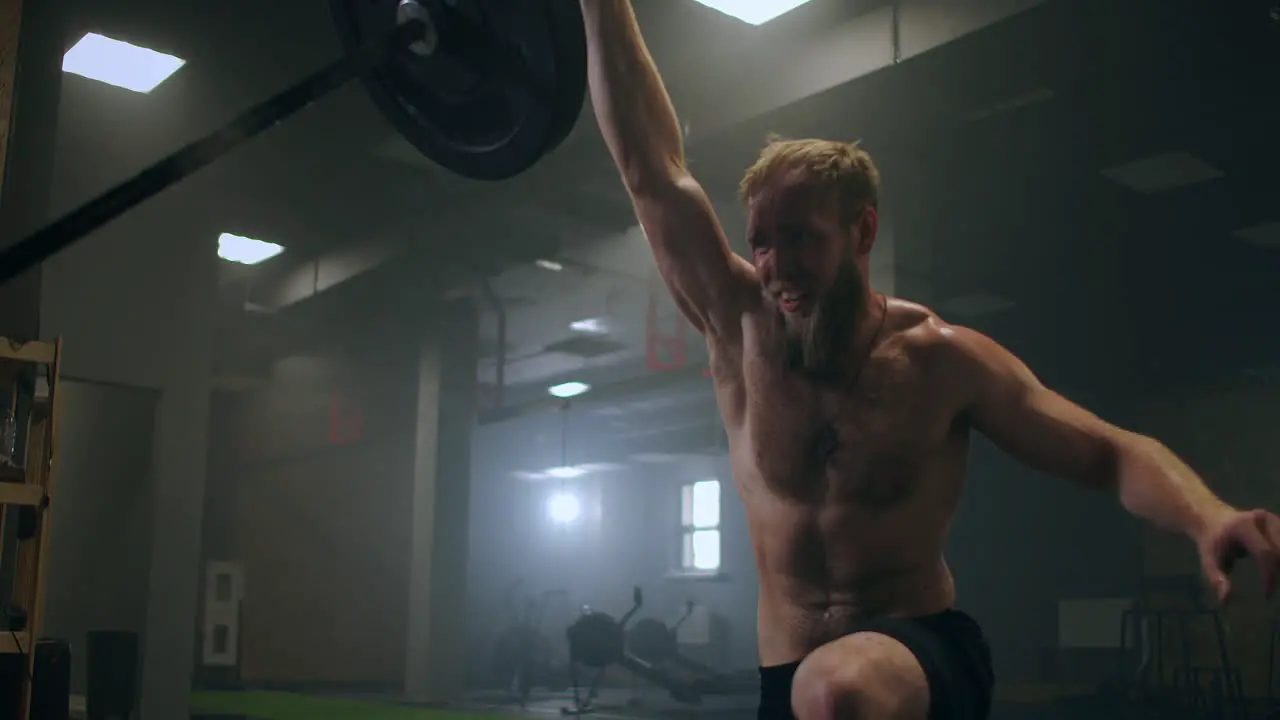 The boy pushes the barbell in the gym with one hand An athlete without a T-shirt in a dark room lifts the barbell while practicing the force of the impact