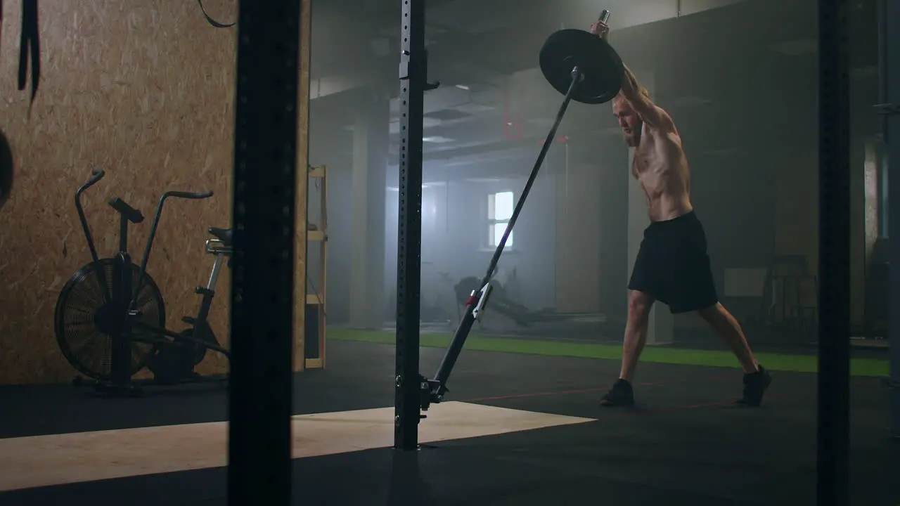 A male fighter working out in the gym pushes a landmine bar with his hand while standing on one knee