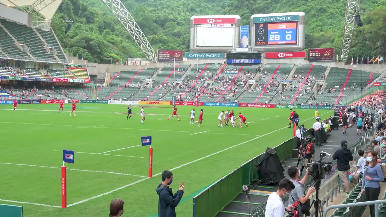 Panning shot of spectators seated in the stadium as a rugby match is ongoing during the Hong Kong Seven rugby tournament after being canceled due to covid-19 government restrictions