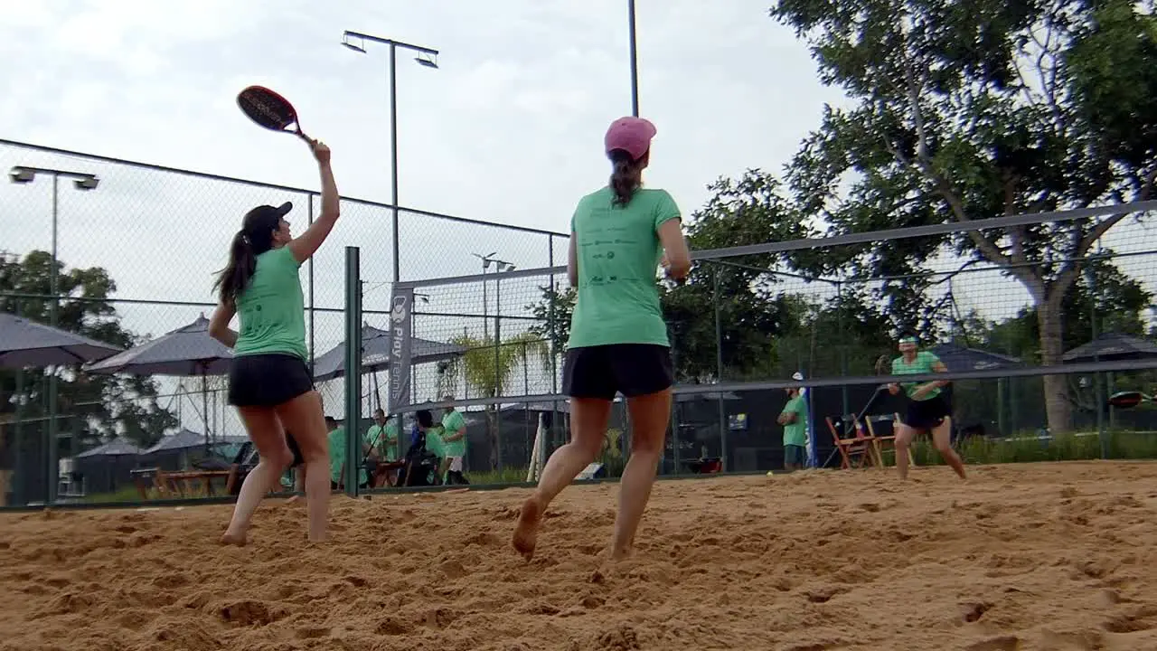 women playing ball in padel match winning a point smashing and jumping on sunny beach padel sandcourt