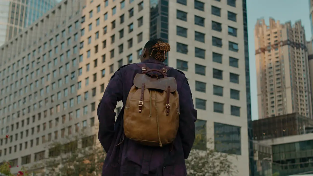 Black man exploring big city with backpack view from behind