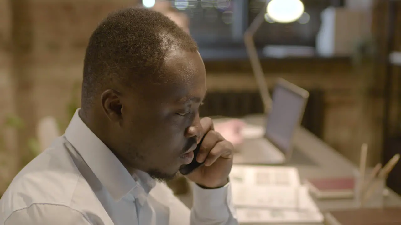 Side View Of American Man Talking On The Phone Sitting At Desk In The Office