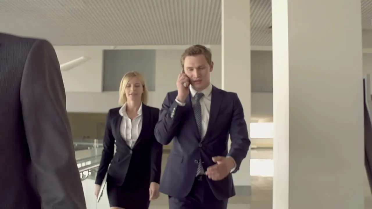 Businessmen And Businesswoman Walking Around The Office One Of Them Talking On The Phone Accompanied By A Blonde Woman