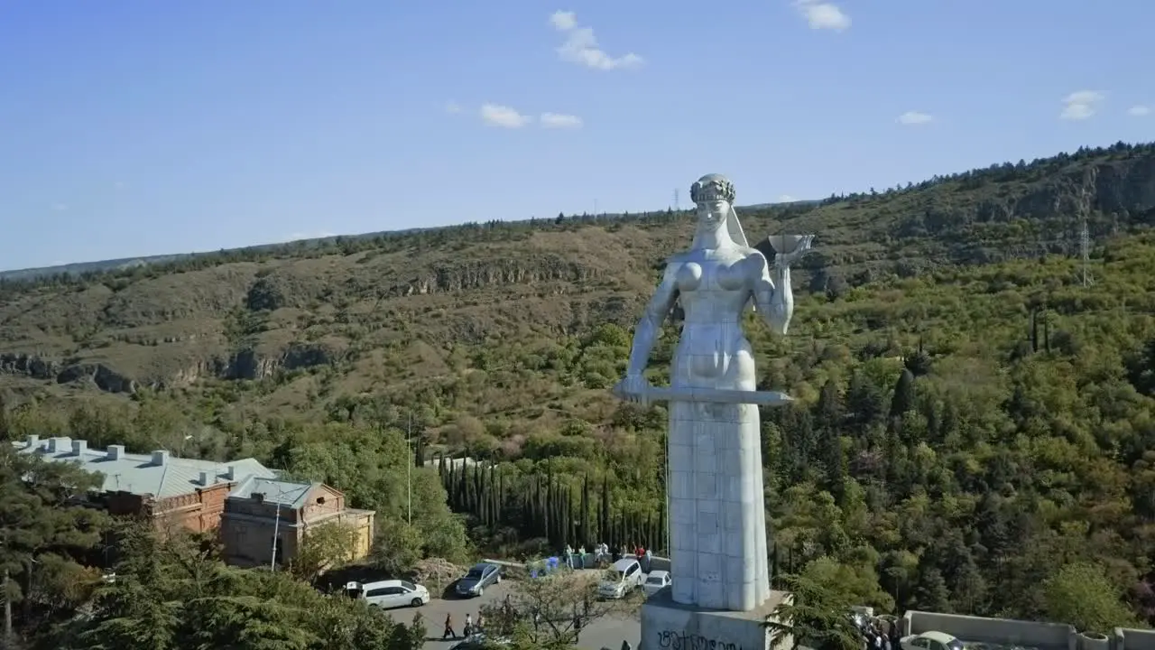 Tbilisi aerial view on a Kartlis Deda monument  autumn view no sun cars passing by old town glass bridge