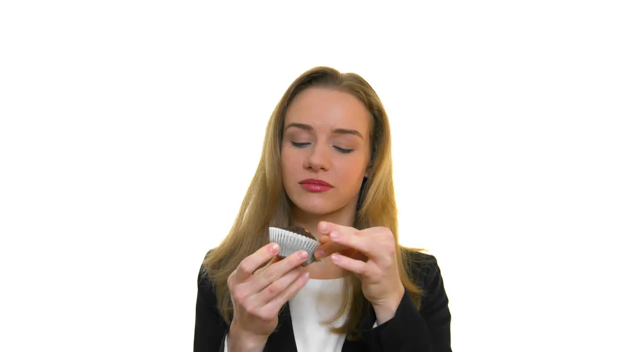 A close-up of a woman smiling and taking a bite out of a chocolate cupcake on a seamless white studio background