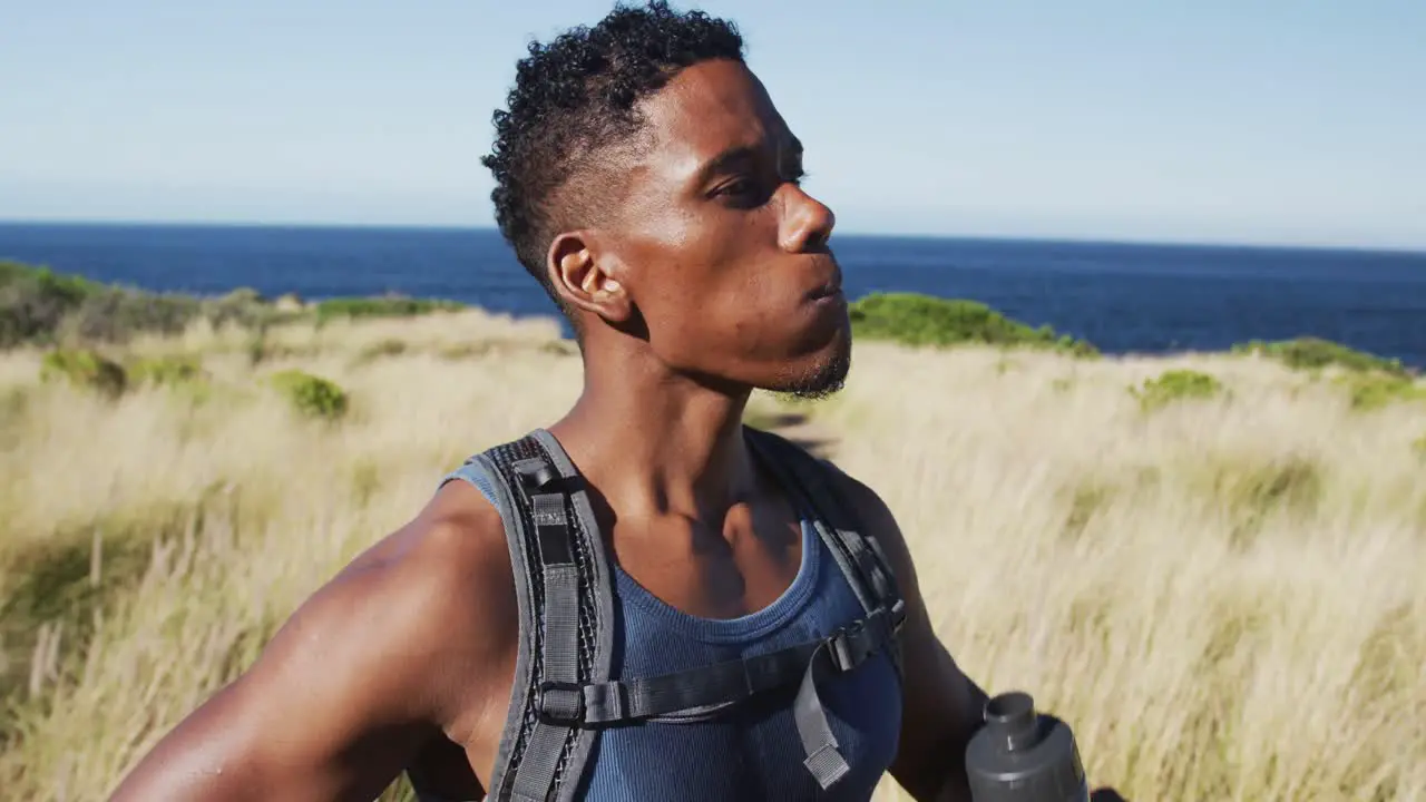 African american man exercising outdoors drinking water in countryside on a coast