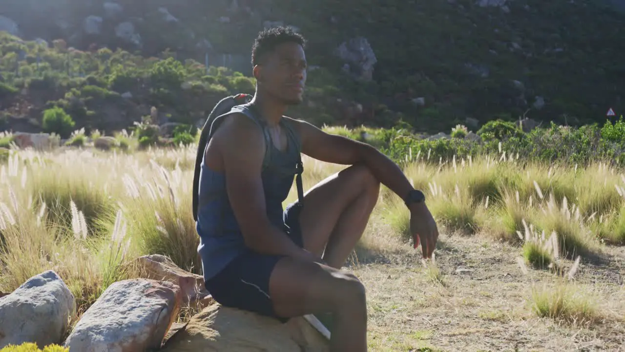 African american man exercising outdoors hiking resting on a rock in countryside on a mountain