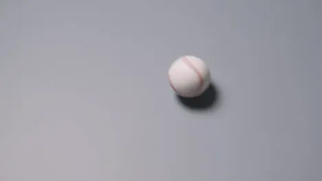 Overhead Shot Of Baseball Ball Rolling Across Frame Against Grey Background