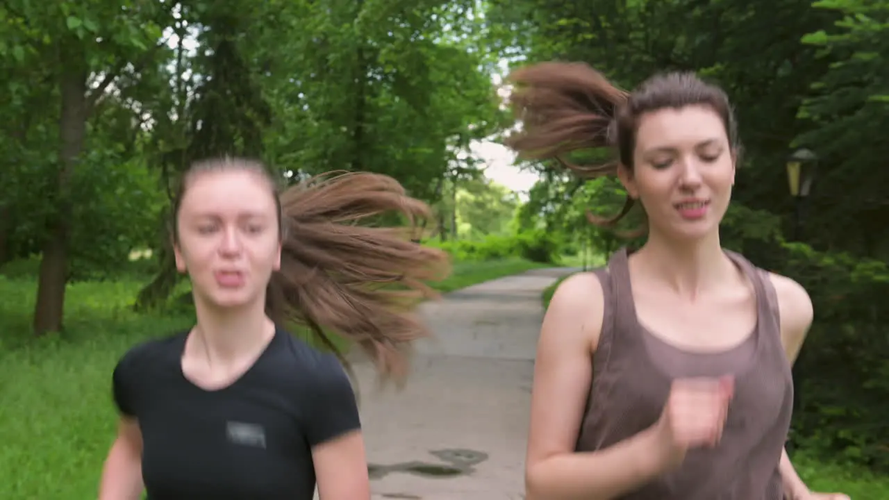 Two Pretty Sportswomen With Ponytail Running Outdoors In The Park