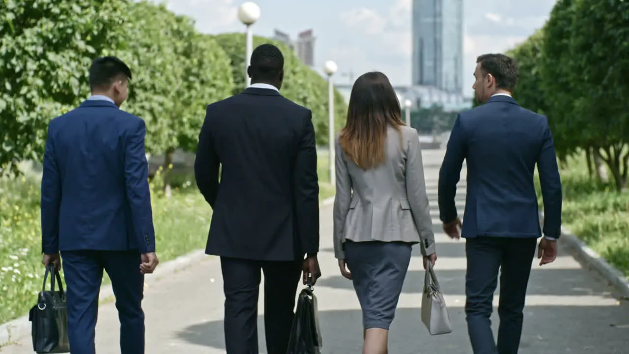 Businessmen And Businesswoman Wearing Elegant Suits Talking And Holding Briefcases While They Walking In The Park