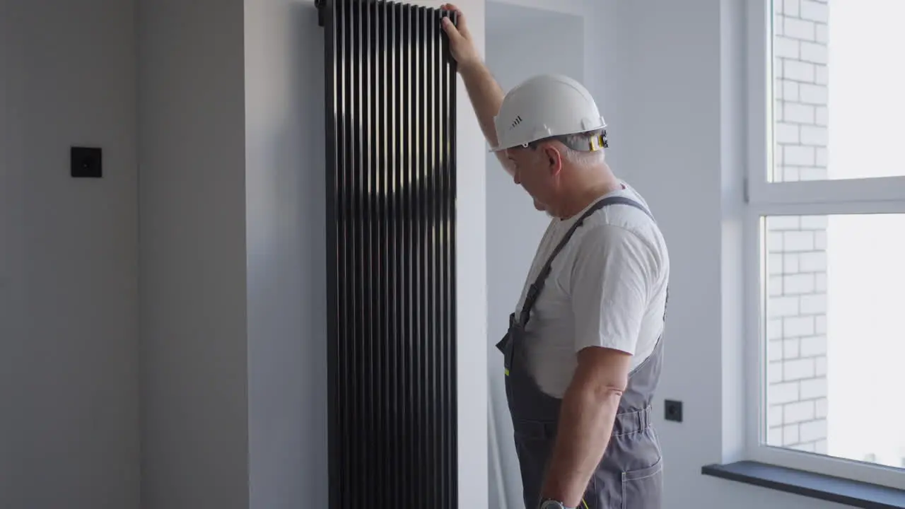 A man plumber in a helmet checks modern batteries for heat output and heating system Heating season