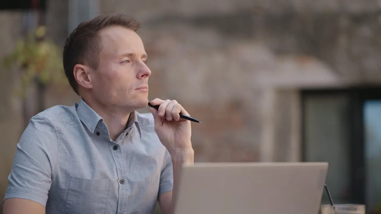 Close-up portrait of ponder young man in office Designer plans his work and holding a pencil in his hand Shooting is slow motion from below Thoughtful serious man sit with laptop thinking solution