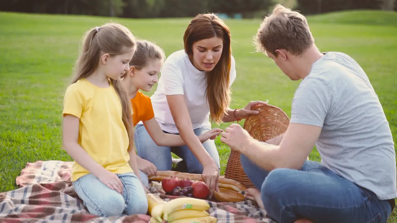 Glückliche Eltern Mit Zwei Kleinen Töchtern Die Essen Aus Dem Korb Nehmen Während Sie Zusammen Auf Der Grünen Wiese Im Park Picknicken