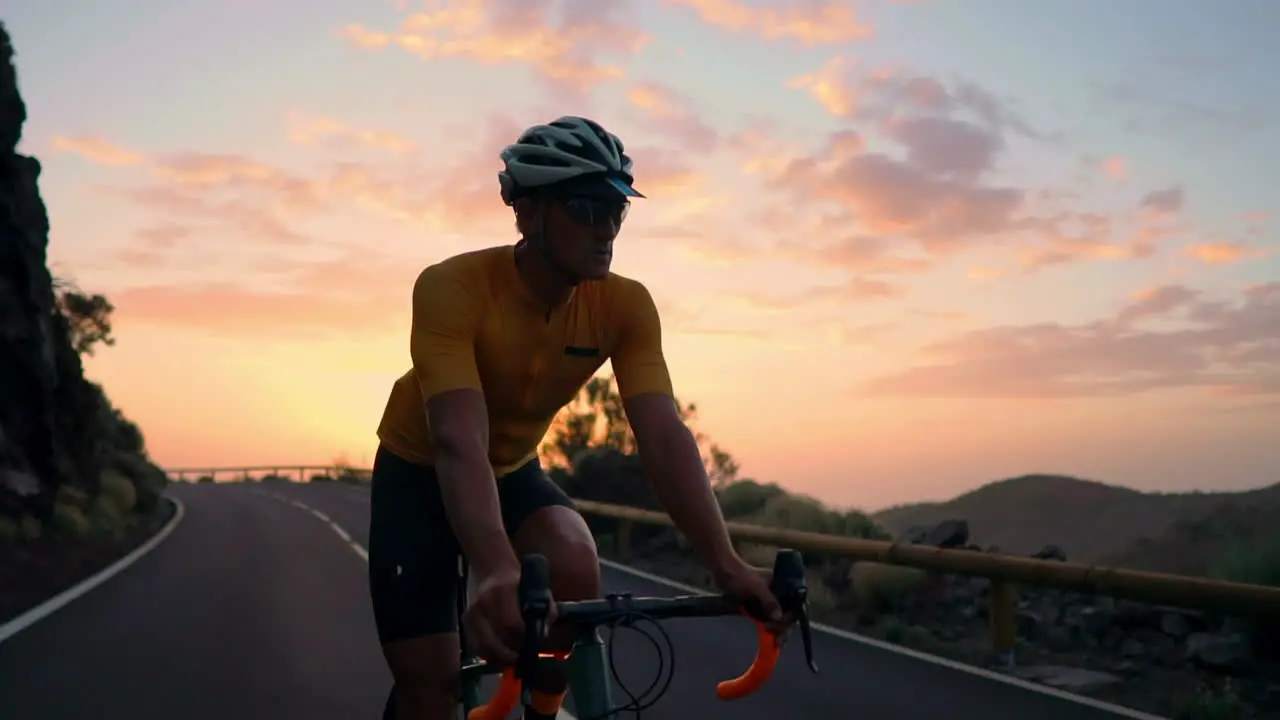 Slow motion captures the athlete navigating a mountain serpentine on a bike taking pleasure in the island's view representing a commitment to a healthy lifestyle at sunset